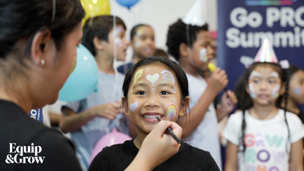 A joyful close-up of a young girl smiling while getting a colorful butterfly painted on her cheek at a children's event.